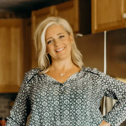 Colleen smiling in a floral blouse in her kitchen.